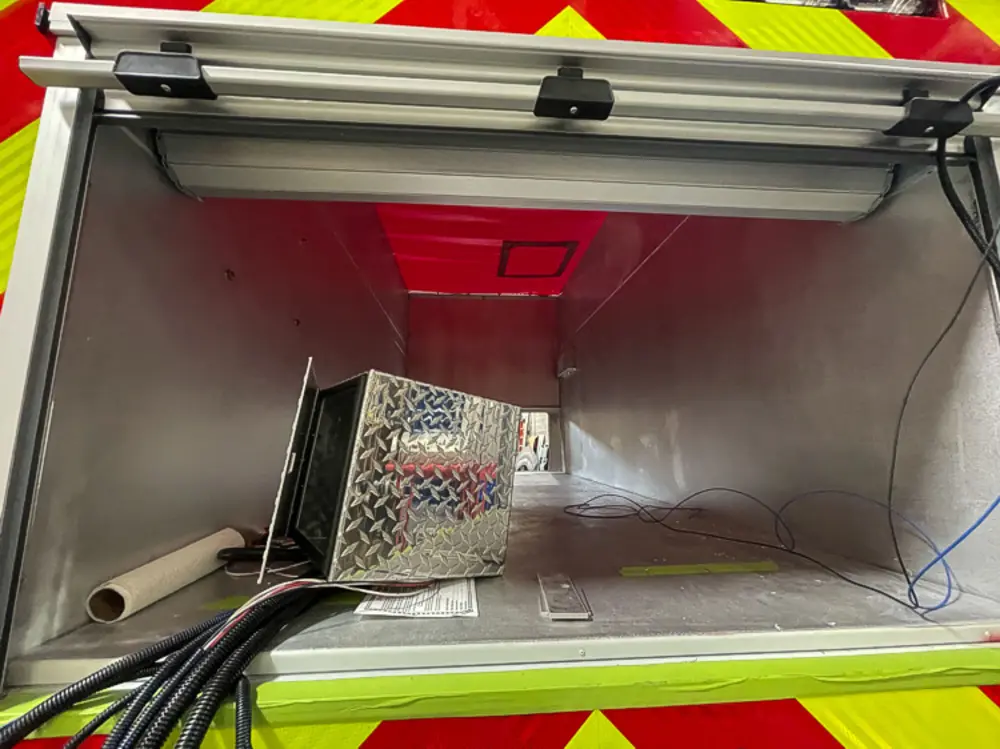 Exterior view of small fire truck showing cab, body compartments, and wheel/tire area.